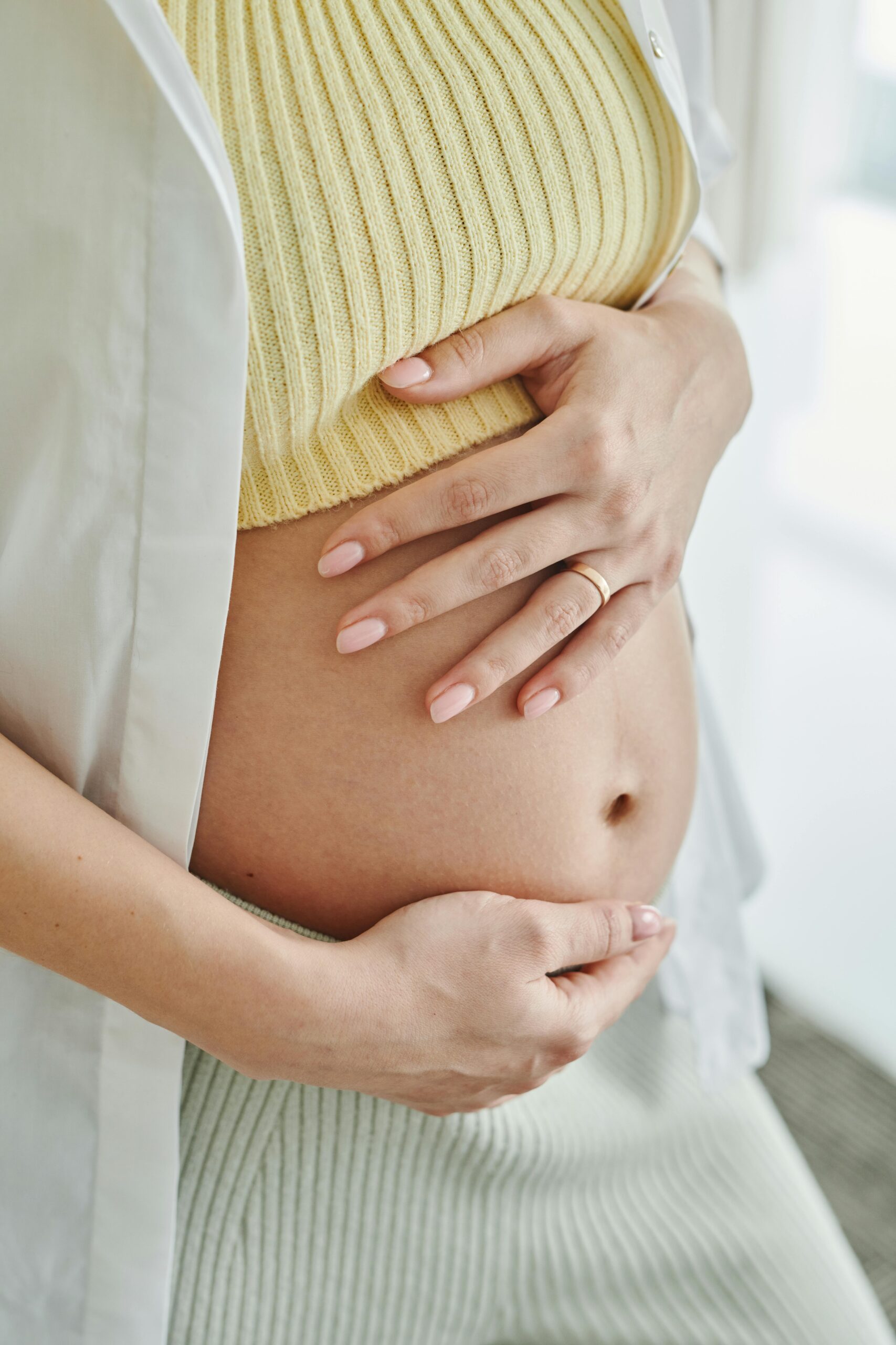 A close-up shot of a pregnant woman's hands gently resting on her belly, symbolizing motherhood.